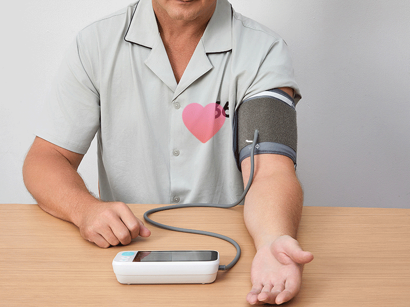 Patient checking blood pressure with a digital monitor, wearing a shirt with a heart logo, promoting regular heart health checks by Dr. Swapnil Garde, best cardiologist in Bhopal.